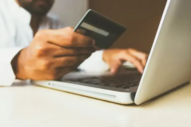Person holding a payment card while shopping online on a laptop