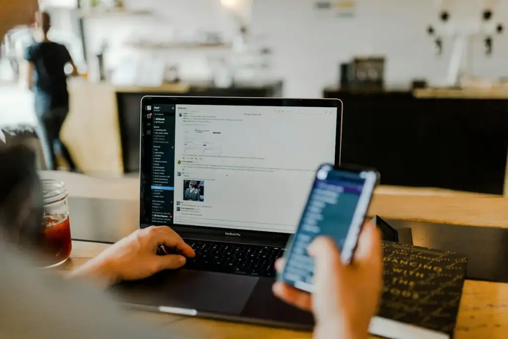 Person using a phone and a laptop at a café table