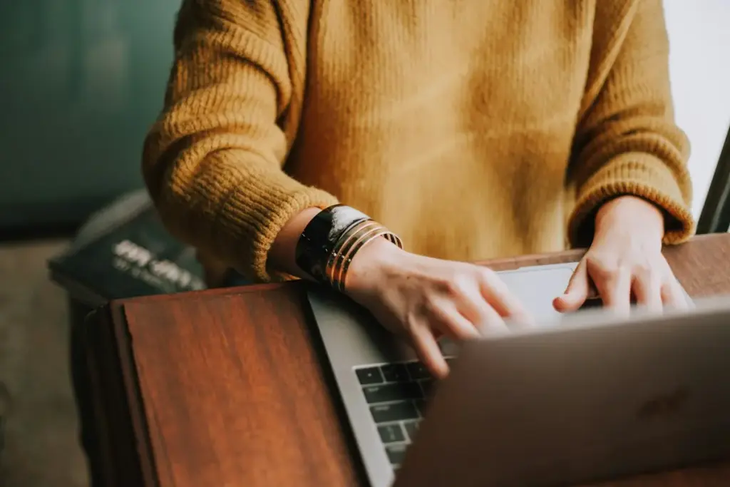 Person typing on a laptop at a wooden table
